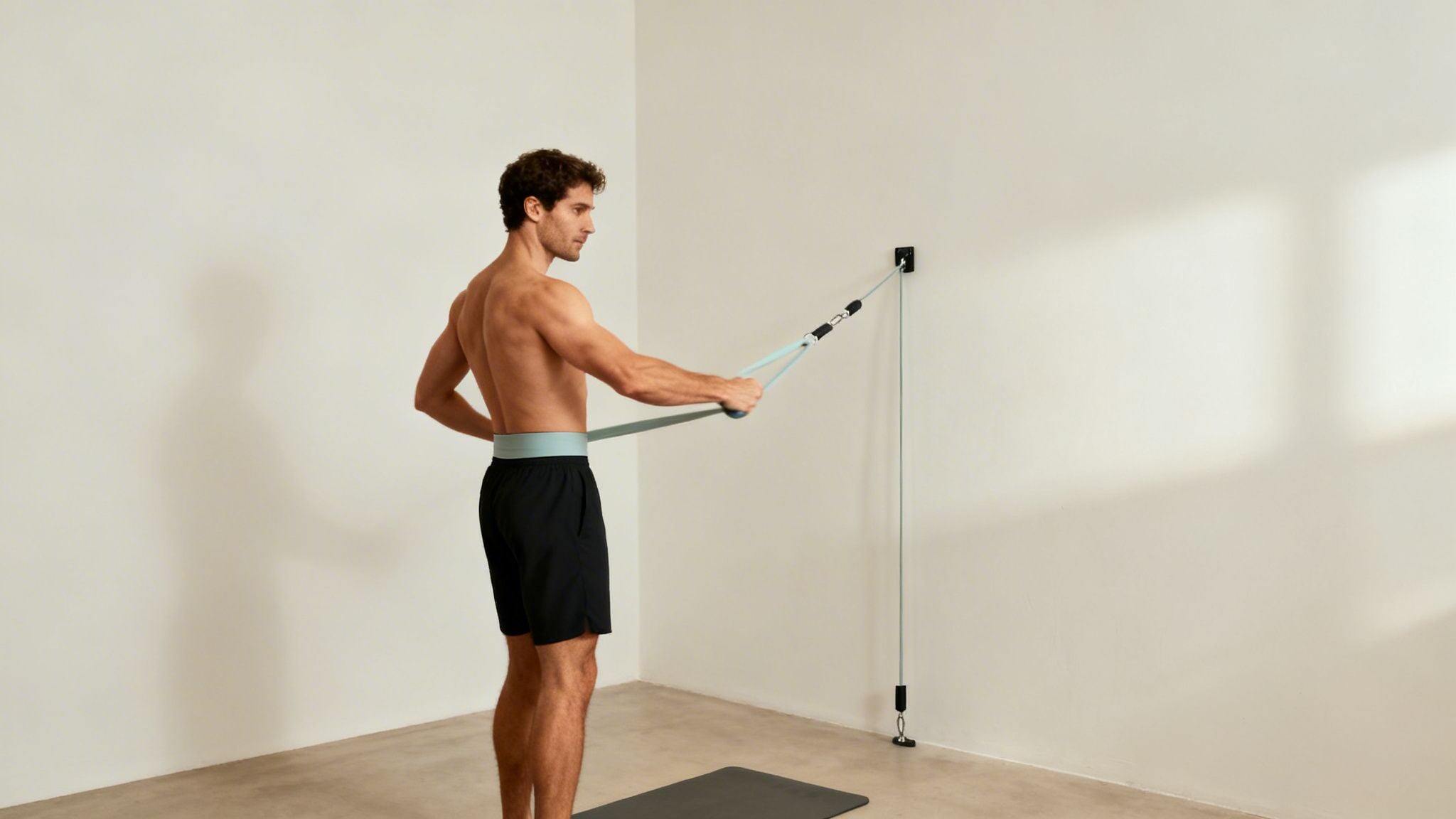 A shirtless man performs a light blue resistance band rotator cuff exercise.