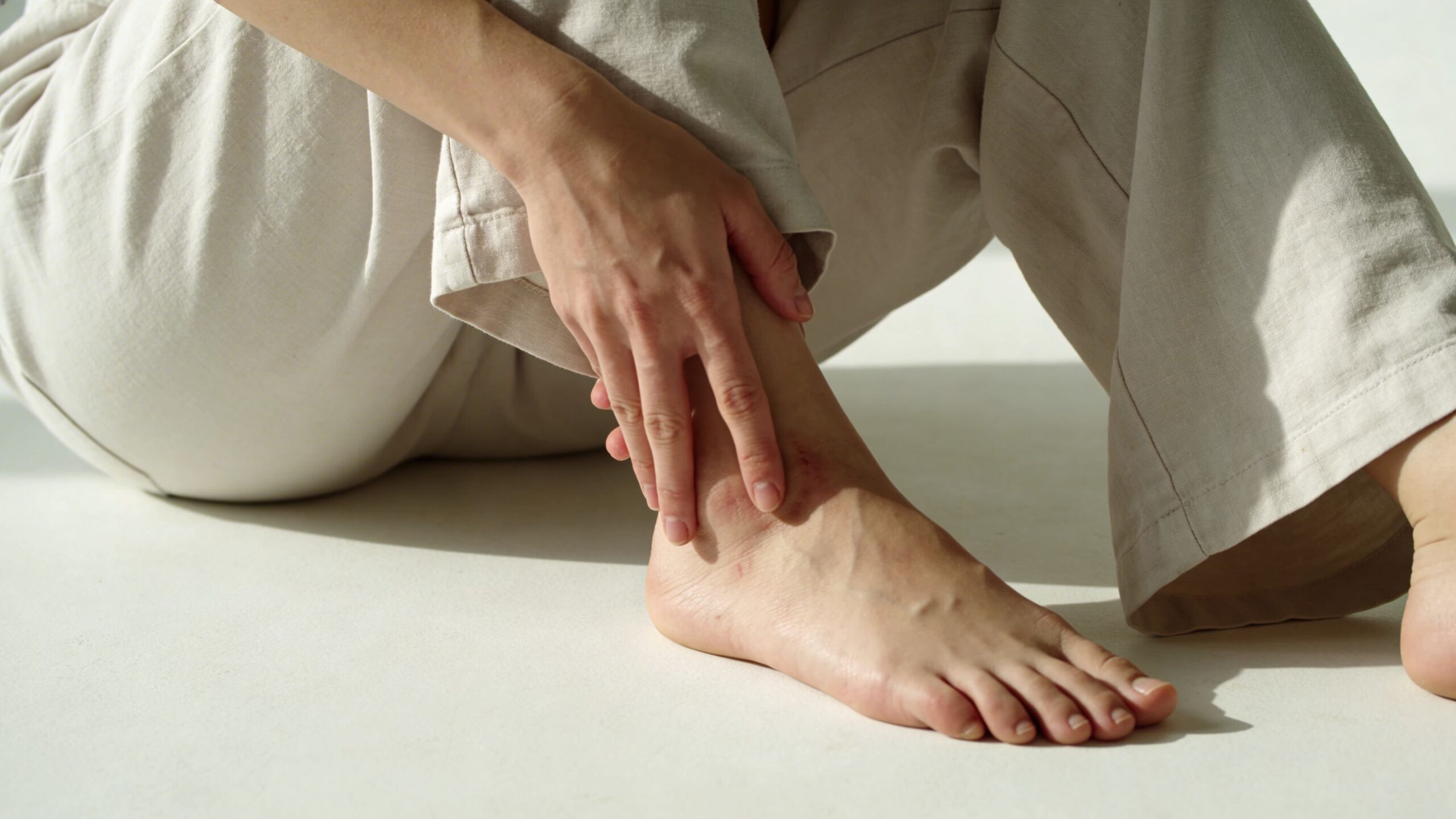 A person sitting down while touching their ankle which shows visible skin irritation and redness.