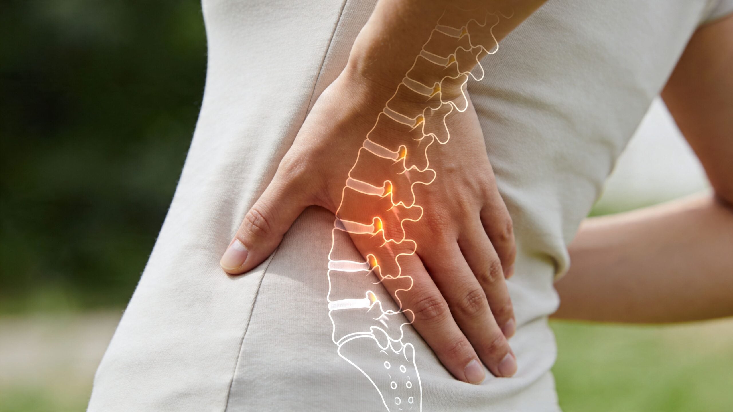 A close-up view of a person holding their lower back with a spinal overlay highlighting inflammation.