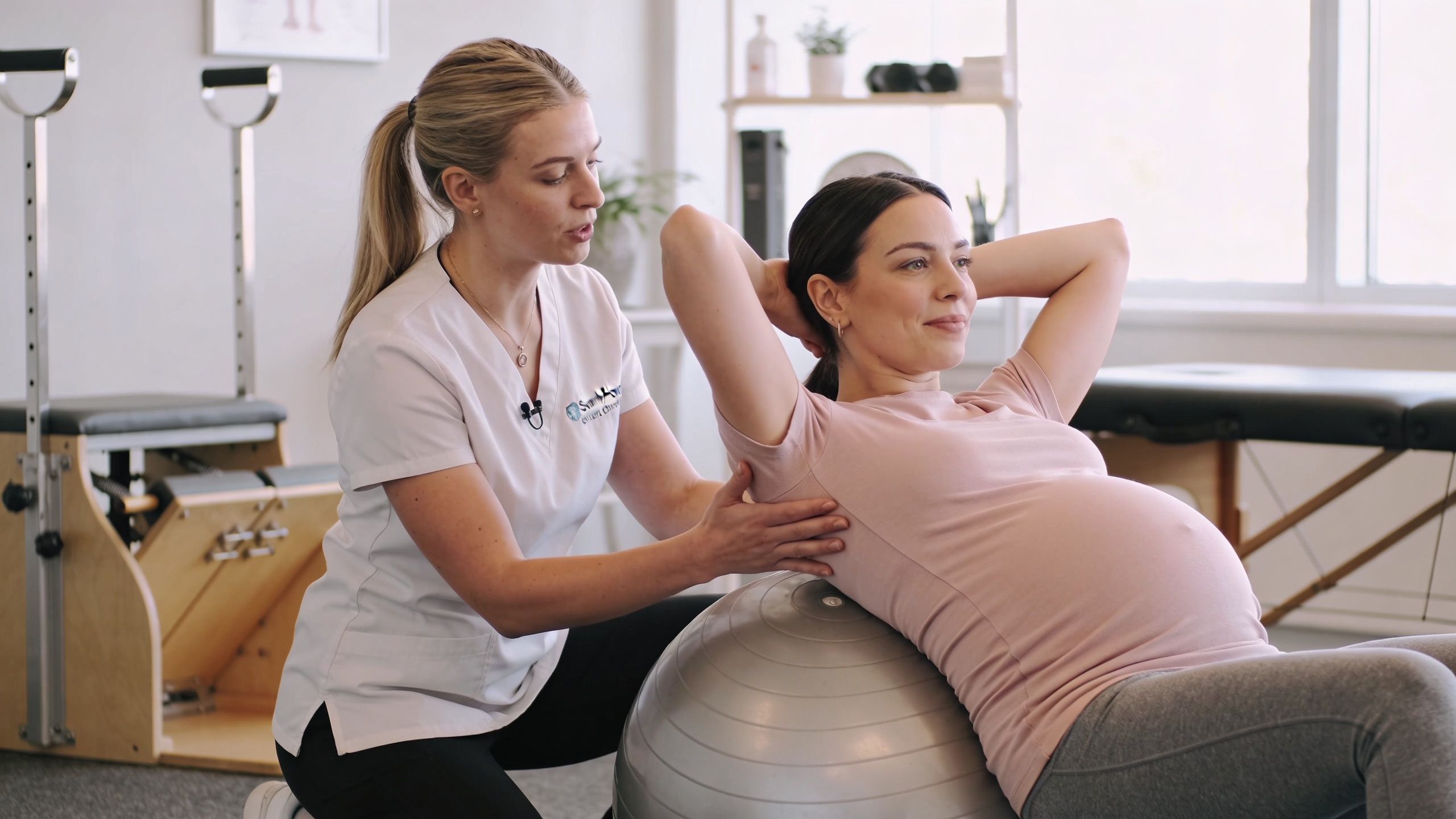 A physical therapist guiding a pregnant woman on an exercise ball during a prenatal therapy session.